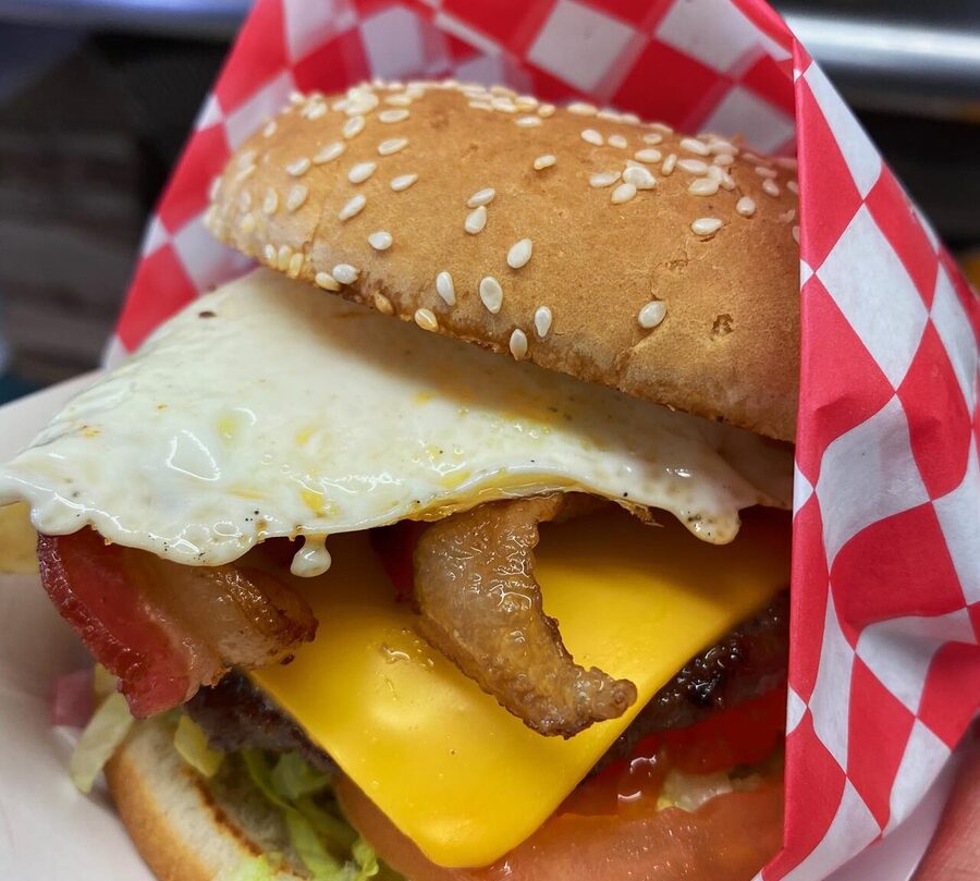 A burger with a fried egg, bacon and cheese, wrapped in red-check paper