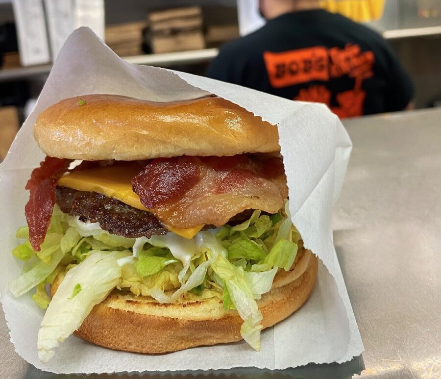 A bacon cheeseburger on the counter, with a crew member in a Bob's tee working behind it